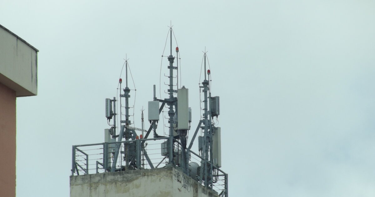 A cluster of 4G and 5G mobile network antennas mounted on the roof of a residential building against a pale sky