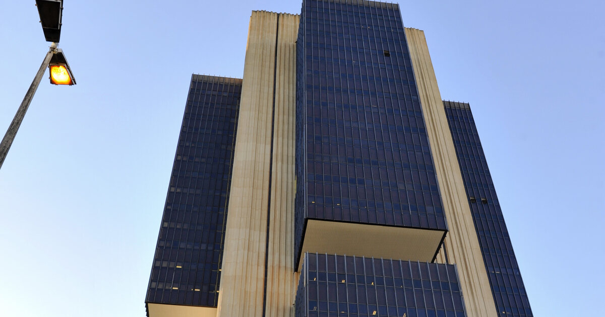 The Banco Central do Brasil headquarters tower in Brasília seen from below against a clear sky, a lit street lamp at the left