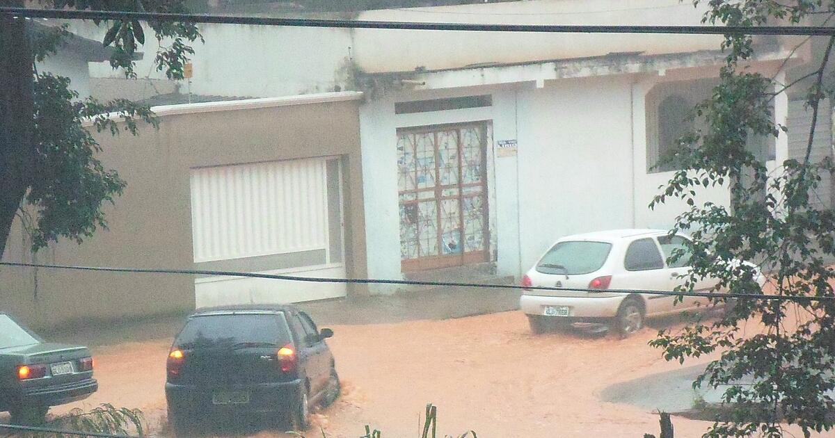 Cars in muddy floodwater on a residential street in Brazil, one crossing with its hazard lights on