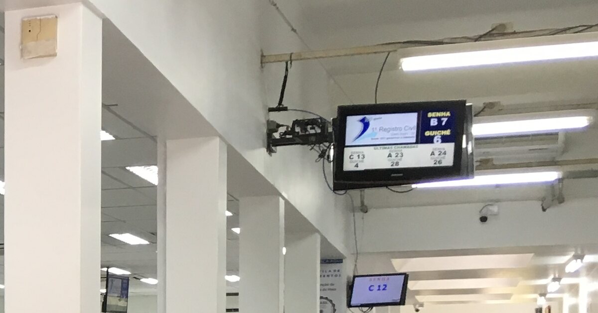 The ticket display in a Brazilian registry office waiting hall, showing the next number and counter above white pillars and fluorescent lights