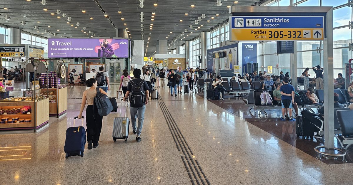 The Terminal 3 concourse at Guarulhos airport, two travellers wheeling their own suitcases, with signs reading Flight connections and Gates 305-332