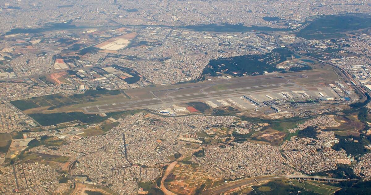Aerial view of São Paulo/Guarulhos International Airport, its two parallel runways and terminal complex with dense city blocks around it to the horizon
