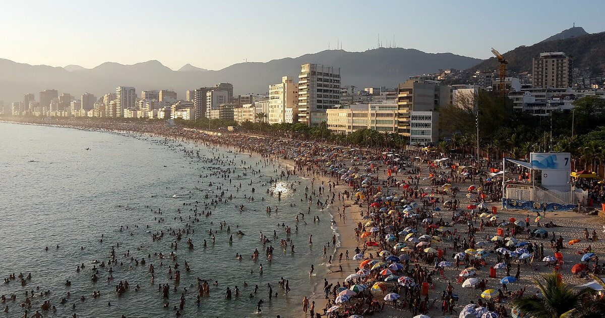Ipanema beach seen from above on a busy afternoon, the crowd stretching along the shoreline with hills behind the city