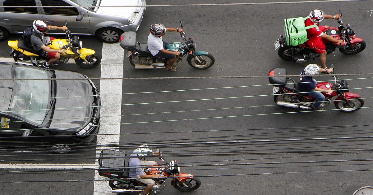 Five motorcycles filtering between lanes at a Porto Alegre junction seen from above, every rider helmeted and one carrying a green delivery box