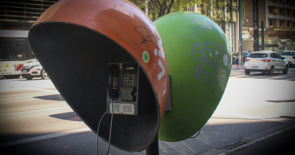 Two Brazilian orelhão payphones on a São Paulo pavement, the front shell open to show the handset and numeric keypad