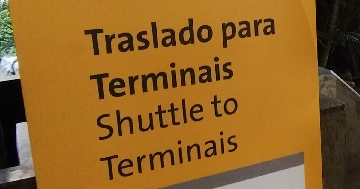 A yellow airport sign at Sao Paulo Guarulhos reading Traslado para Terminais above the English line Shuttle to Terminais