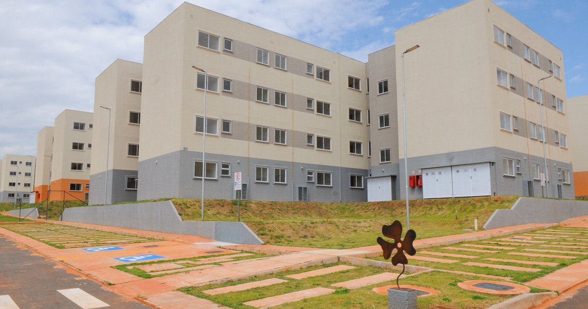 A four-storey residential block in Brazil seen from the street, with plain painted facades, garage doors at ground level and an empty paved forecourt