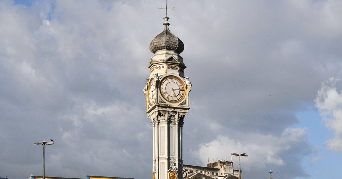 The white cast-iron clock tower on Praça do Relógio in Belém, its gilded dial and onion dome against heavy clouds
