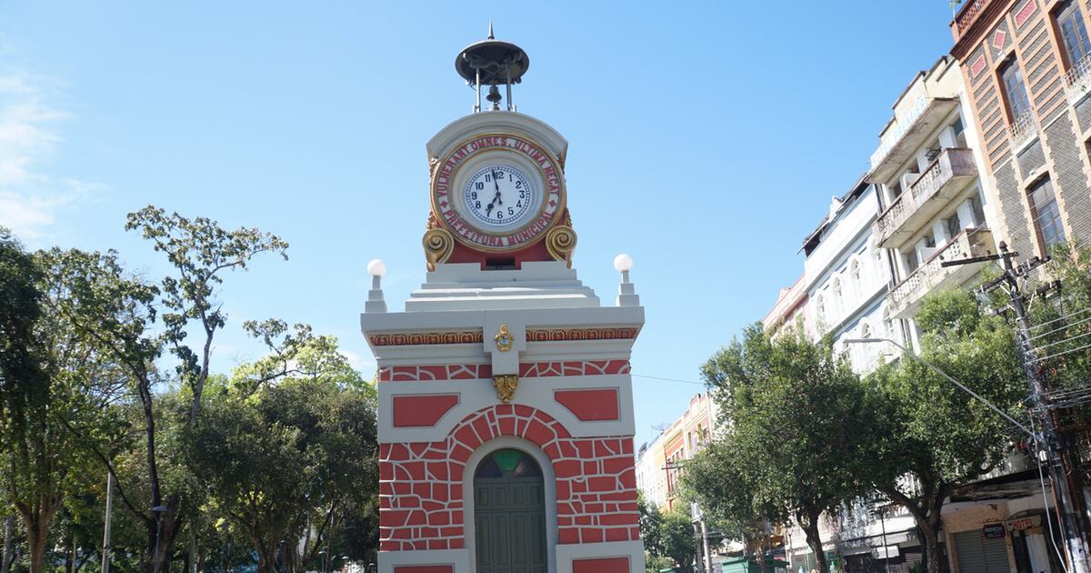 The red-and-white municipal clock kiosk in the historic centre of Manaus, its Latin motto ringing the dial beneath a bell canopy