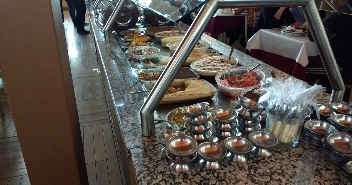A Brazilian buffet counter lined with serving dishes and small bowls, tables set behind it