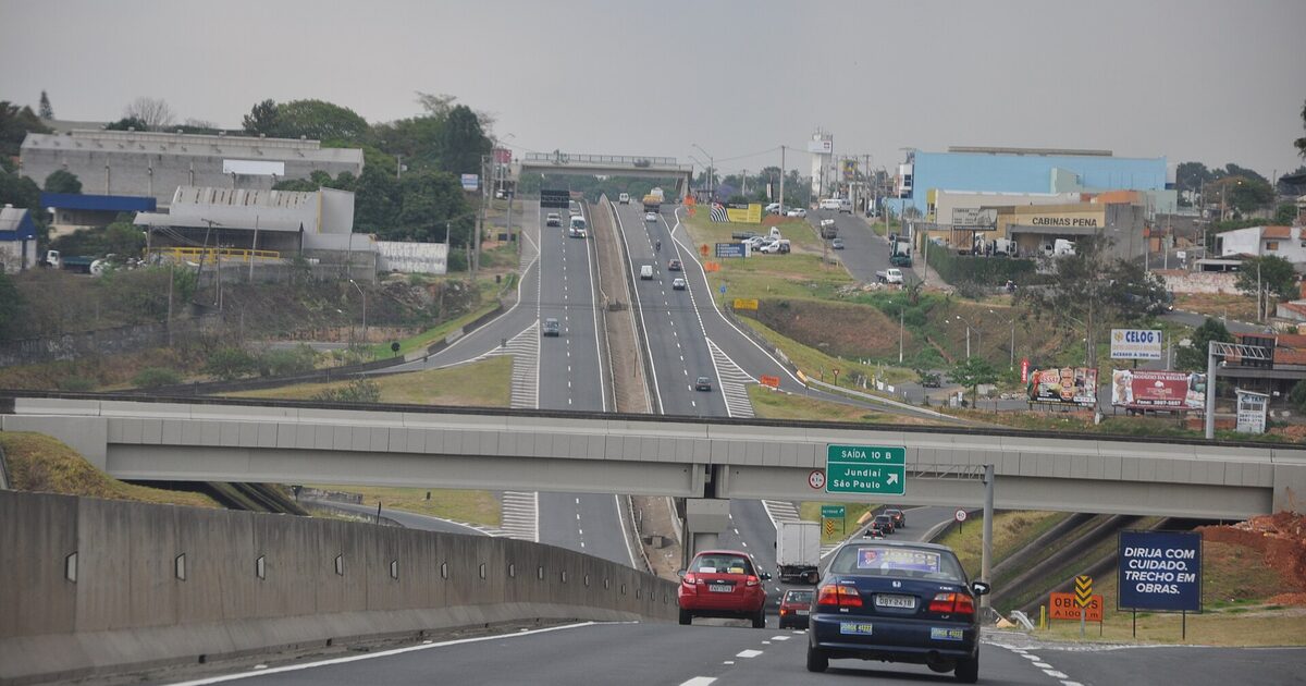 A dual-carriageway Brazilian motorway seen from a moving car, an overpass and green direction signs ahead