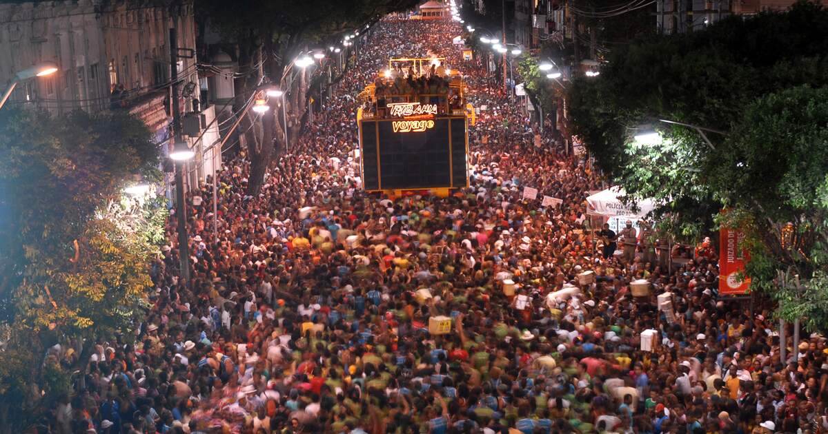 A dense crowd fills a street behind a trio elétrico, the sound truck that leads Salvador's street Carnival, seen from above at night